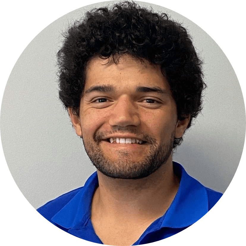 Staff photo of Logan Dolbel Thomas, wearing a checked blue and white shirt in front of a plain grey background.