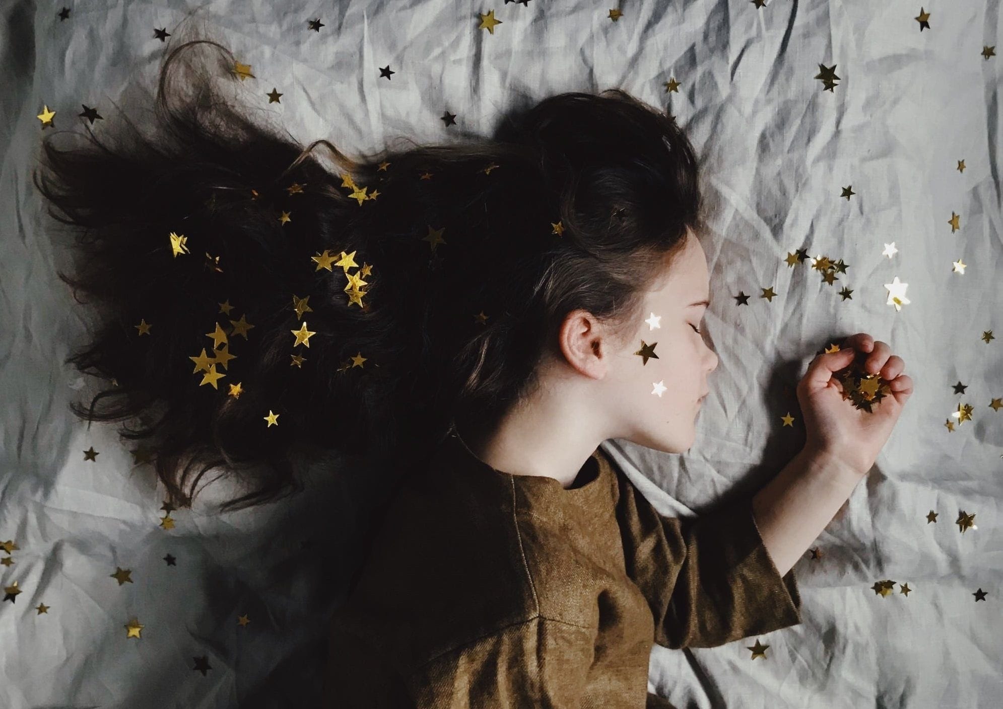 Child sleeping on her side, with stars sprinkled around the bed.